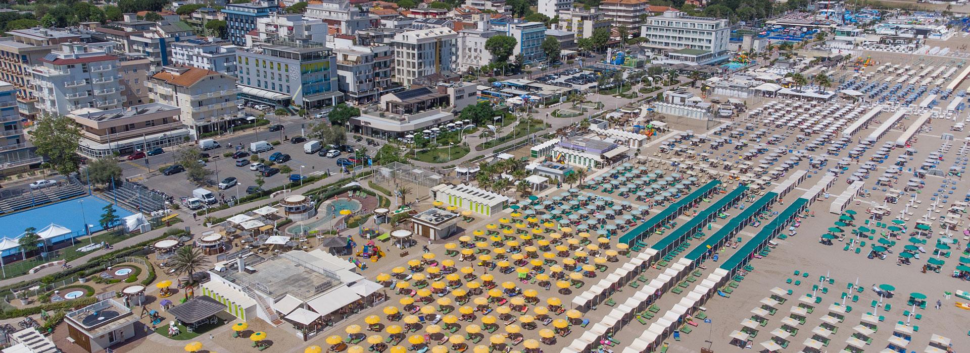 Spiaggia affollata e colorata, ombrelloni, vivace città sullo sfondo.