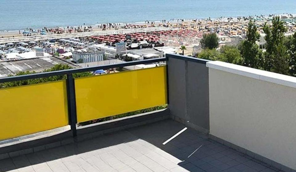 Vista mare da un balcone soleggiato, spiaggia affollata e ombrelloni colorati.